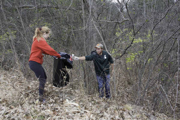 two students remove litter from a wooded area