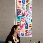 Bridget Shearon sits with one of her photography projects on display behind her. The photos capture images taken through a microscope lens. Lilly Kujawski | Washtenaw Voice