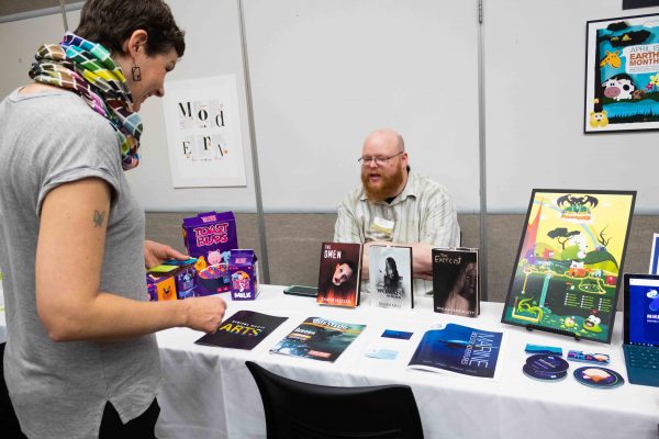 Janna Kryscynski (left), a student who works at the production center, talks to Mike Lovelace about his graphic design projects at the Digital Media Arts Gala. Lily Merritt | Washtenaw Voice