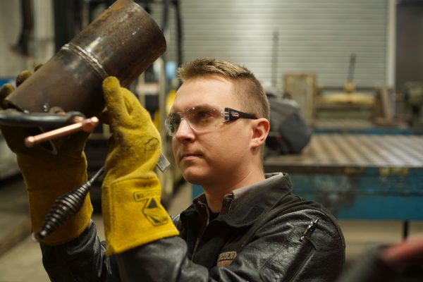 Alexander Pazkowski, a welding instructor at WCC, brushes away on a cylindrical piece of metal. Torrence Williams | Washtenaw Voice