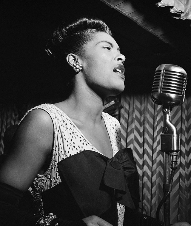Billie Holiday is shown in black-and-white singing into a microphone.
