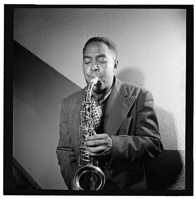 Charlie Parker is shown in black-and-white playing the saxophone and wearing a pin-striped suit.