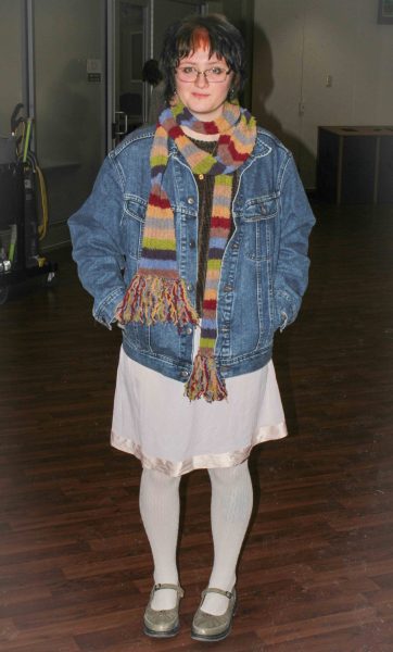 Emma Akio wears a warm rainbow scarf & denim jacket over a light pink dress & white stockings with a pair of grey Mary Janes.