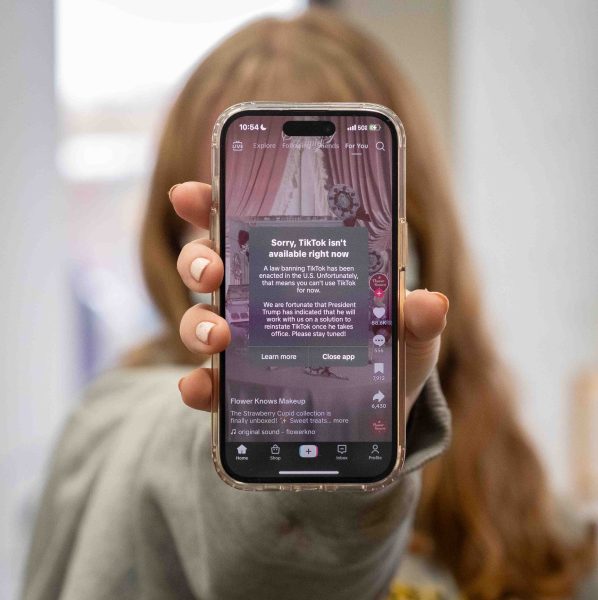 A close-up of a person's iPhone being held in front of them. A notification shows that the TikTok app is unavailable.