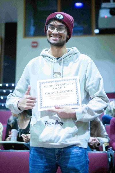 student Owen Lazenby stands with a smile and a thumbs-up while holding a newly won Accountability Award