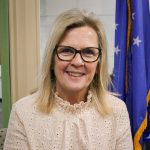 headshot of Carol Osborne from the shoulders up smiling with an American flag in the background