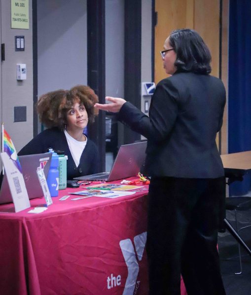 A seated representative speaks with a standing participant, with the table standing between them.