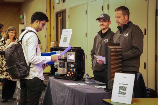 A student reads a flyer while standing in front of a table with two representatives.