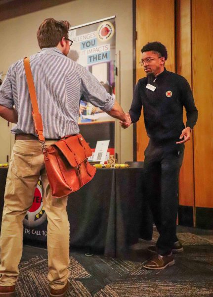 A participant and representative step to the side of the table to shake hands and greet one another.