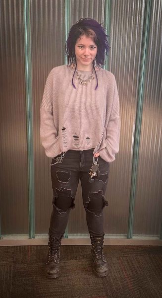 Photo of Cece Roe in front of a silver wall, wearing a grey distressed sweater and ripped black jeans with combat boots.