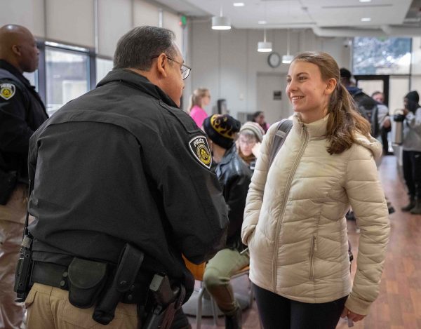 A student wearing an off-white coat speaks with Officer Paul Gomez.
