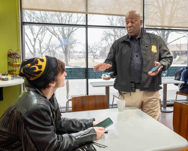A student sits at a table, holding their phone in their hands, and listens to Deputy Chief Derran Shelby answer a question.