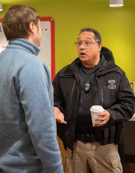 A student stands with his back to the camera while speaking with Officer Paul Gomez.
