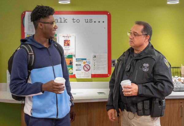A student speaks with Officer Paul Gomez while they both hold cups of coffee.