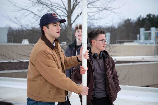 Two students hold a PVC pipe upright and look into the distance. Another student points at the tower from the behind.