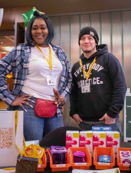Kathy Gray and Mike Wallace pose for a picture together behind their Harm Reduction Outreach table.