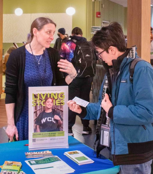 Molly Ledermann and Isaac Salomon chat together at the Bailey Library Table. Salomon holds and reads a flyer.