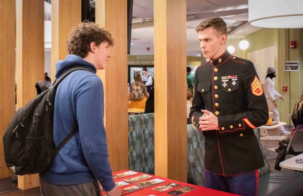 Andrew Whitebell speaks with Marines Sergeant William Knight, who stands behind a table in uniform.