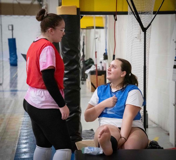 Lainey Varney stands and talks to Hannah Wiles who sits and ices an injury.