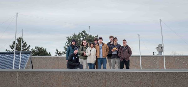 The students pose on the roof for a group photo with their instructor. They are proud of their work building the radio tower.