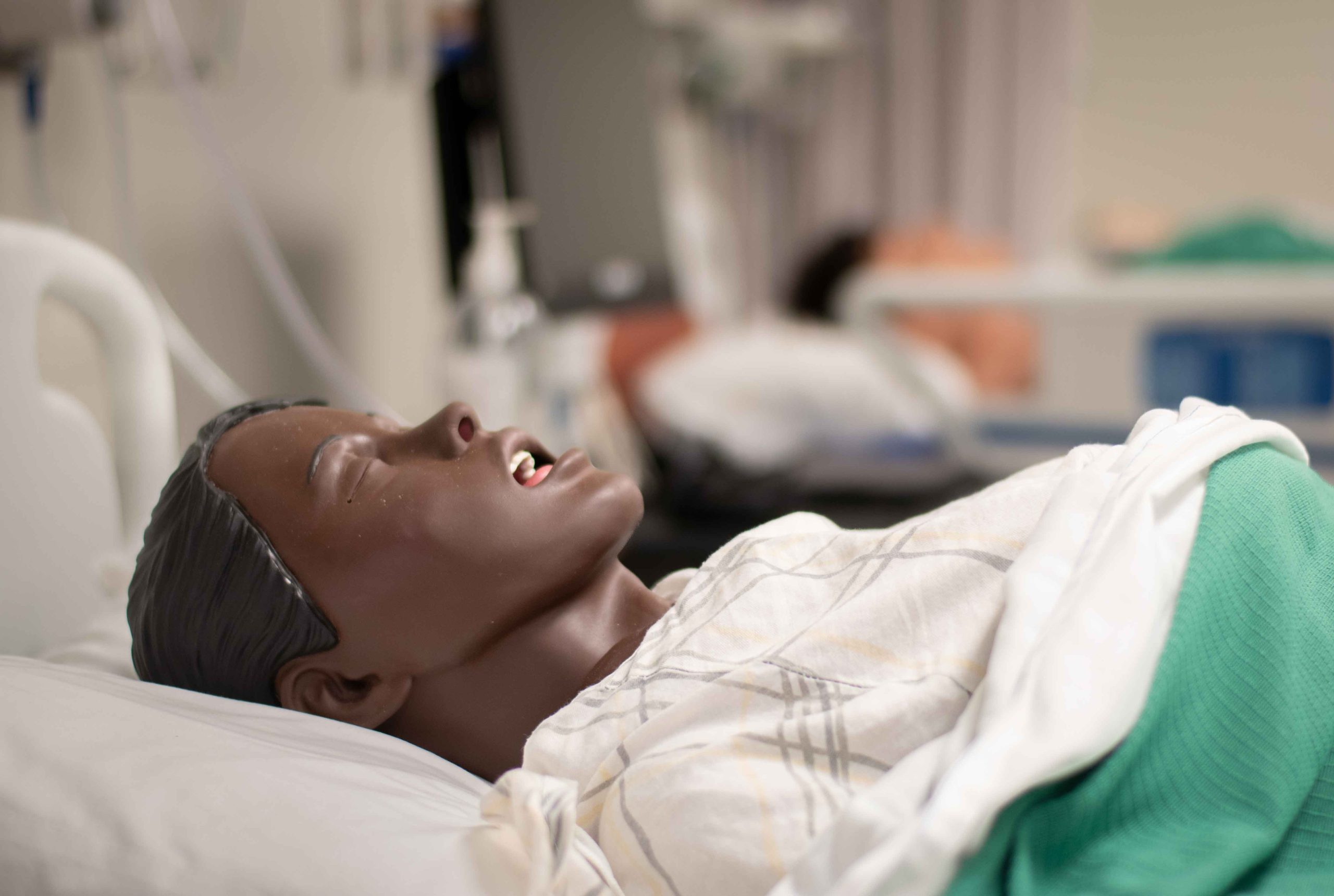A close-up of a nursing mannequin laying face-up in a bed.