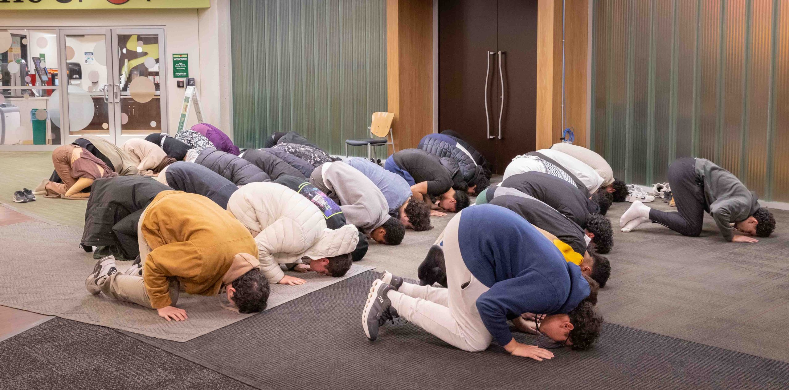 Four rows of Muslim students kneel with their feet, hands, and foreheads touching the ground while they pray.