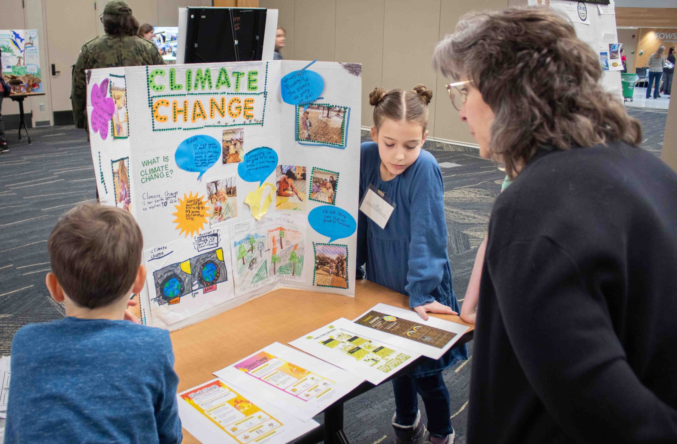 Two elementary students wearing blue shirts present their Climate Change poster to an attendee.