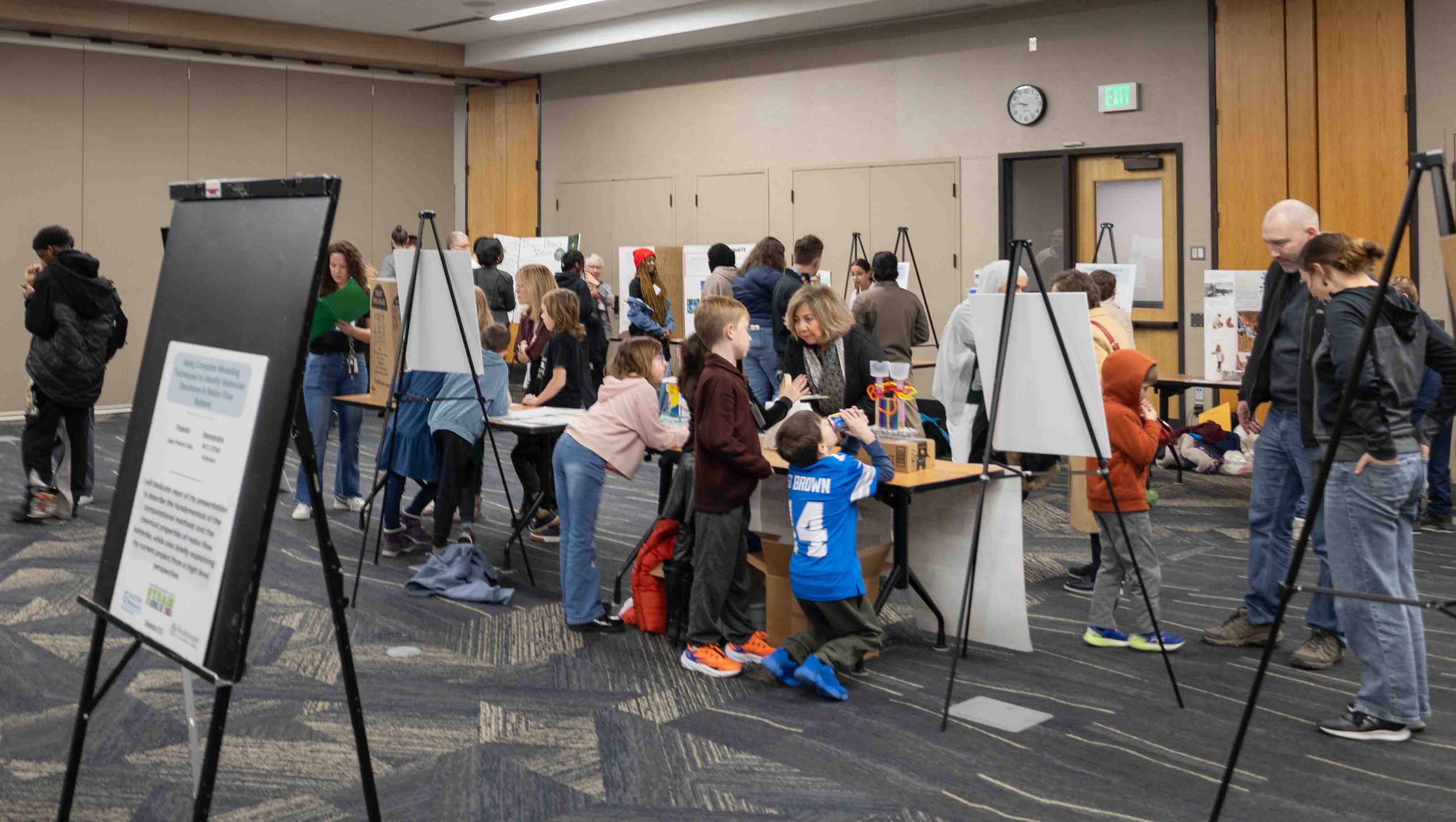A wide-shot photo of the STEAM event elementary school student section. College students present their work behind them.