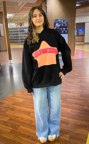 Joslyn Quintana-Aguirre wears a black hoodie with an orange star, light-wash jeans, and white tennis shoes.
