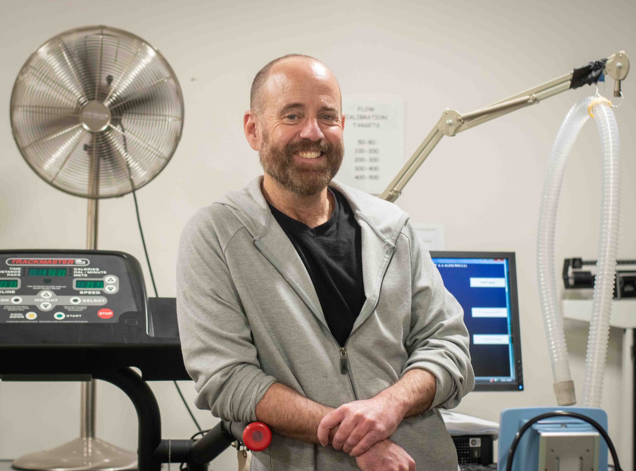 Patrick Johnson is shown smiling and leaning against a treadmill from the waist up.