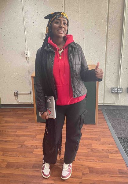 Ines Mato is shown wearing a silk headscarf, black jacket over a red hoodie, black jeans, and brown and white Nike sneakers.