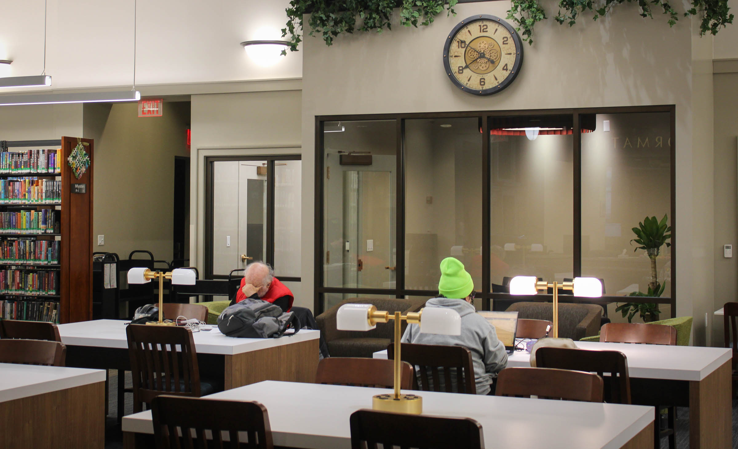 Two people sit at the new white tables inside the Ypsilanti Library. Each table has a shiny gold lamp.