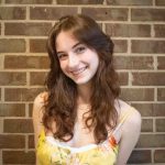 Headshot of Katie Ulinski smiling and tilting her head toward the left. She wears a yellow tank top.