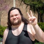 Keaka Cagle is shown from the chest up, wearing a black tank top and smiling while posing with hands making a peace sign.