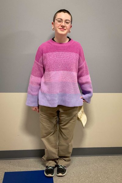 Martina Reading Sunol wears a striped sweater fading from pink to purple with tan pants and black sneakers.