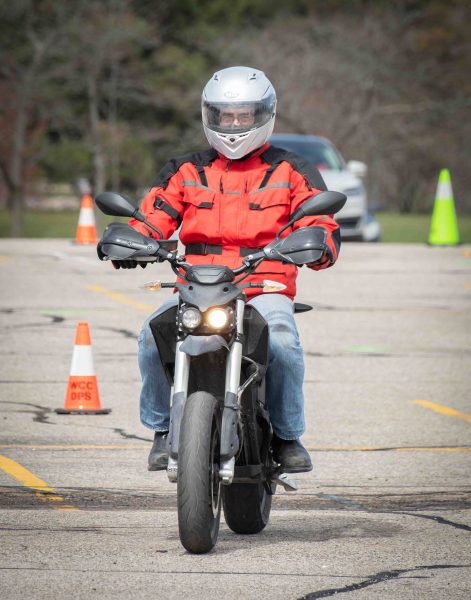 Andrew King is shown on his motorcycle driving towards the camera. He wears a white helmet and red jacket.