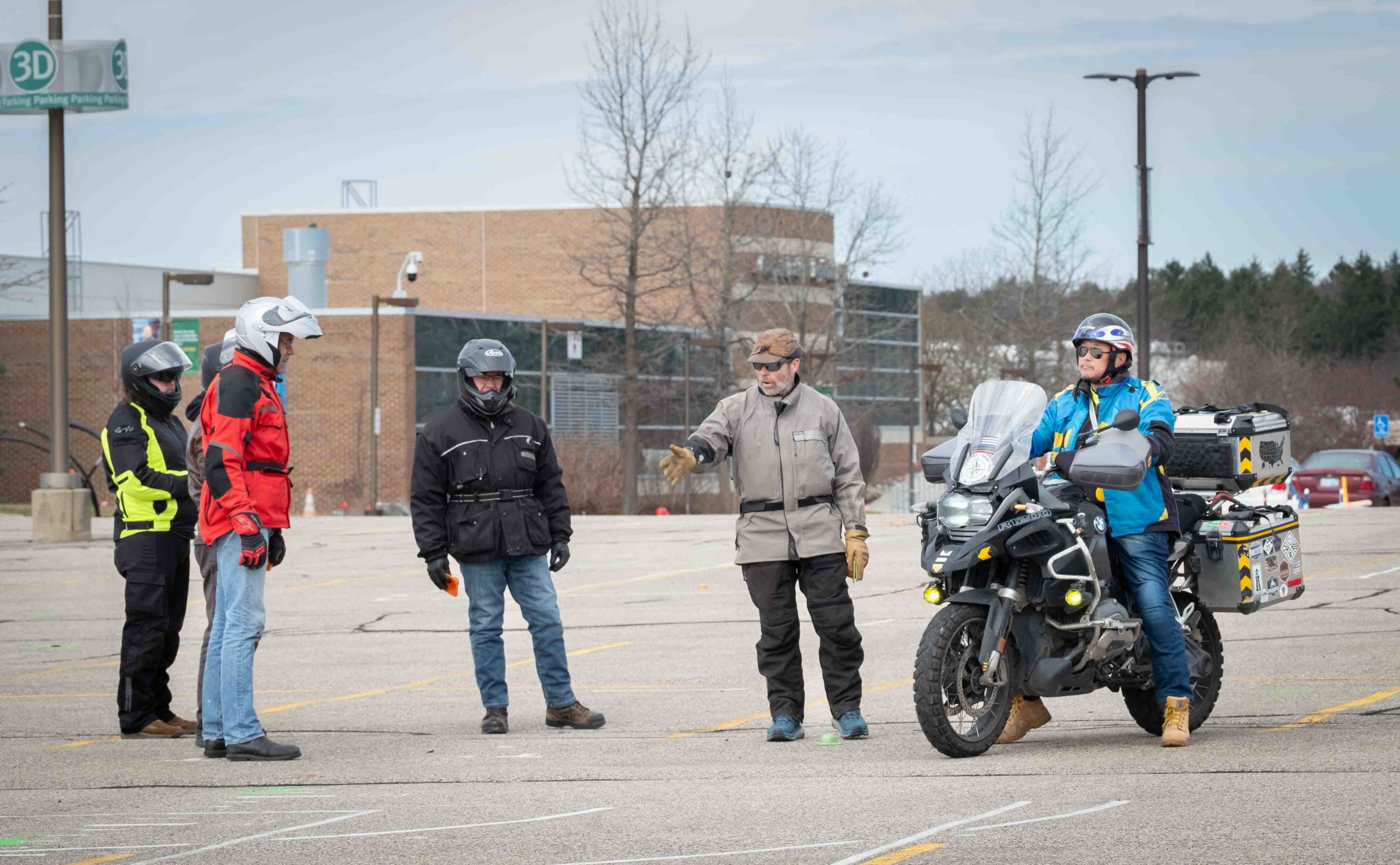Five people stand in the parking lot while another sits on a motorcycle.