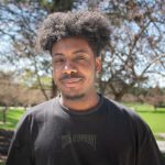 Headshot of Nelson Portis smiling without teeth and wearing a black T-shirt.