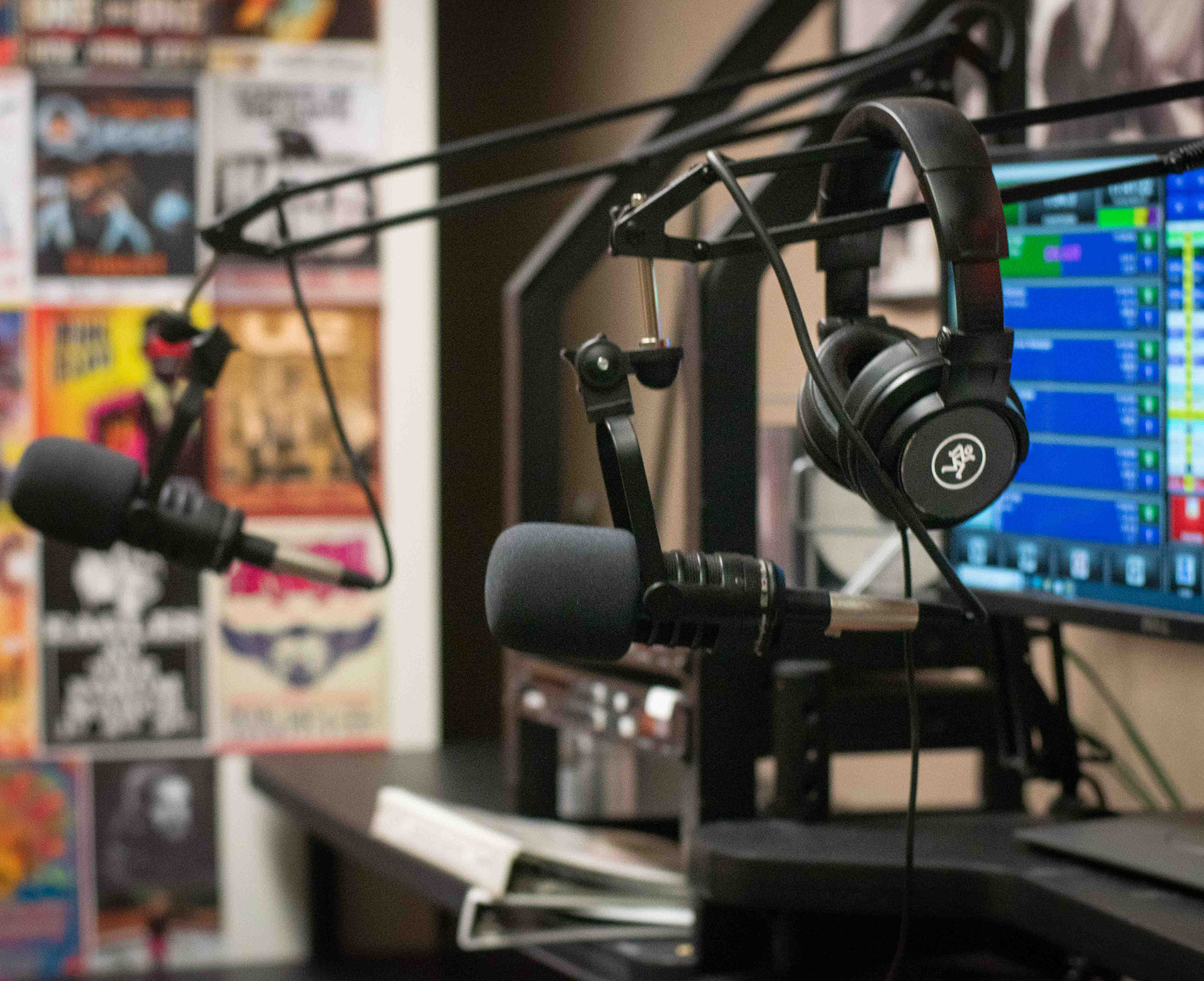 Two microphone stands rest on a desk. A pair of headphones is hooked onto one.