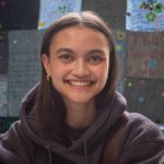 Headshot of Samantha Dark, smiling and wearing a grey hoodie and gold earrings.