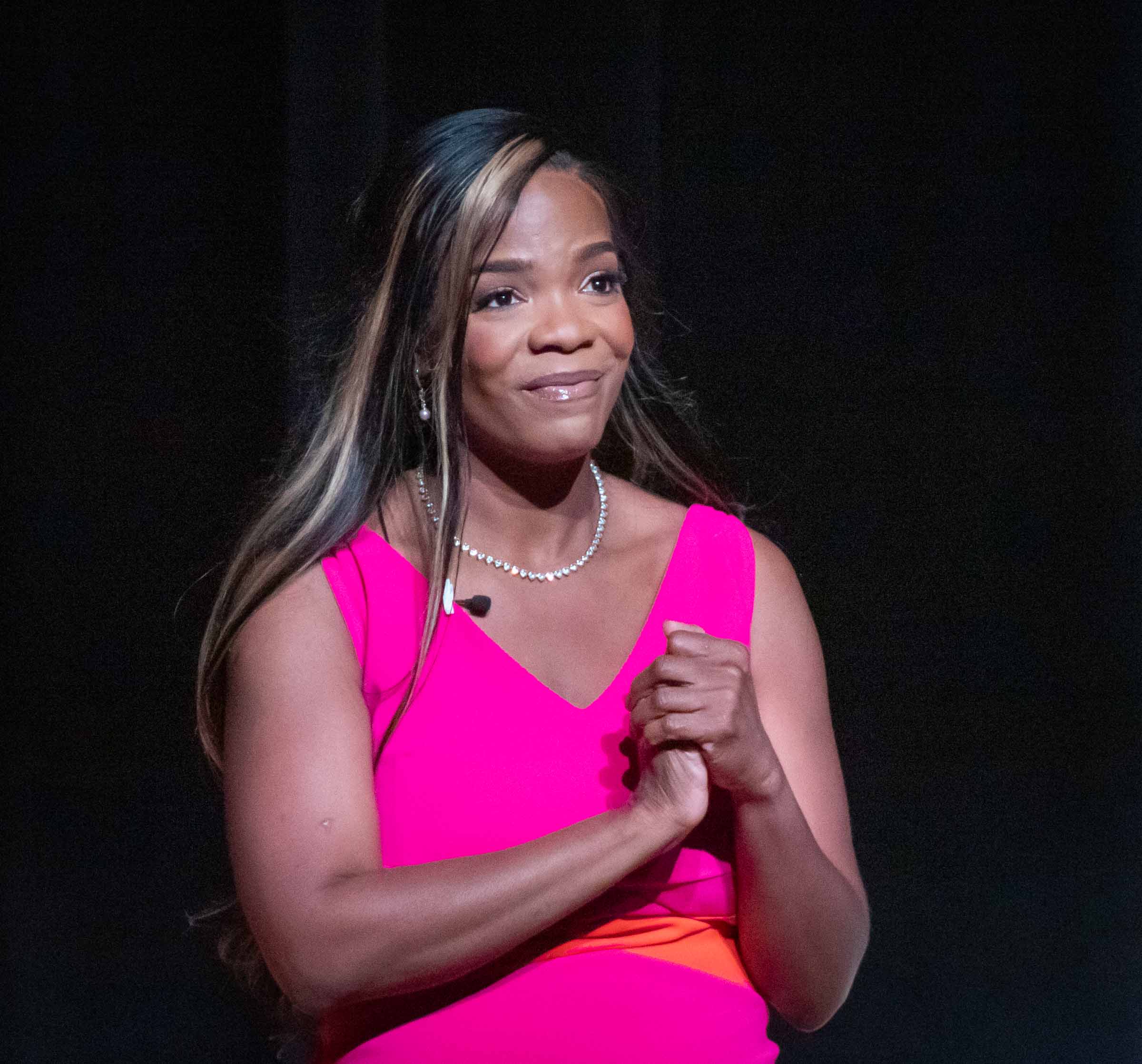 Michelle Silverthorn is shown from the waist up with her hands clasped together. She wears a bright pink and orange dress.