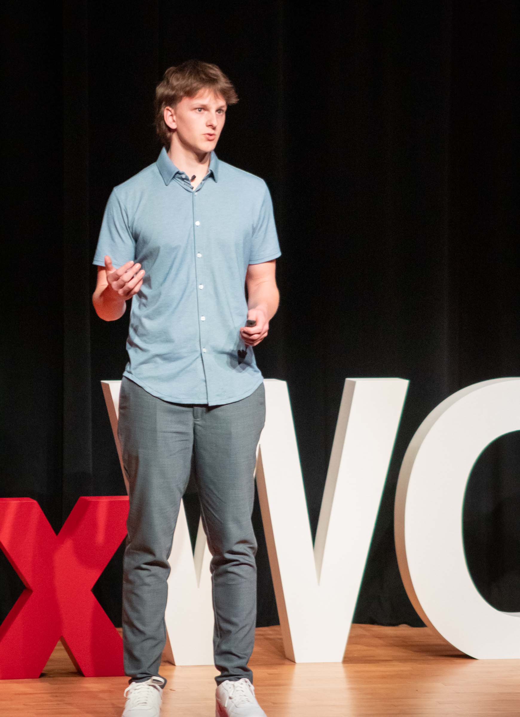 Roman Karas uses hand gestures while speaking to the audience. He wears a blue dress shirt and gray slacks.