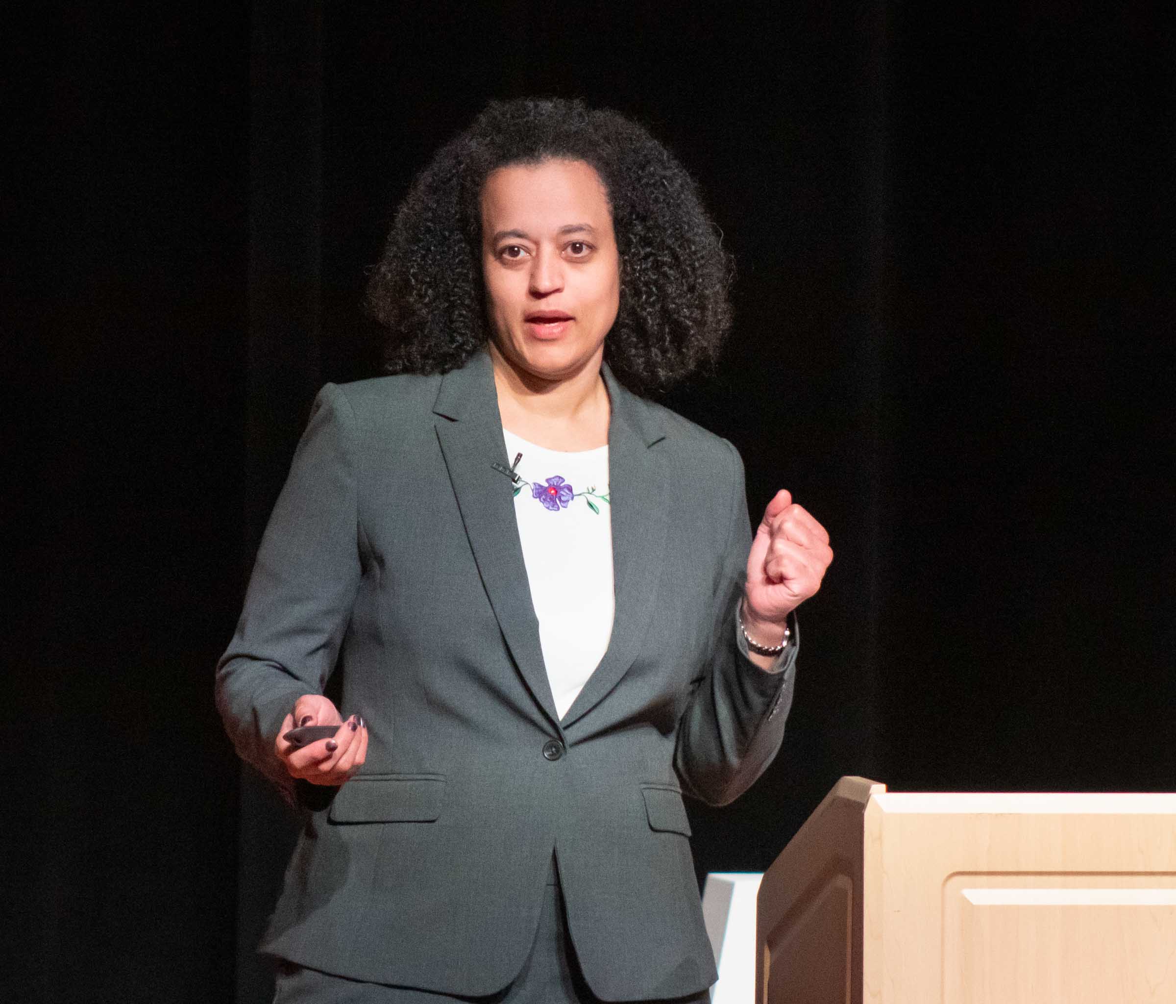 Jennifer German is pictured from the waist up while speaking to the audience. She wears a gray suit and white blouse.
