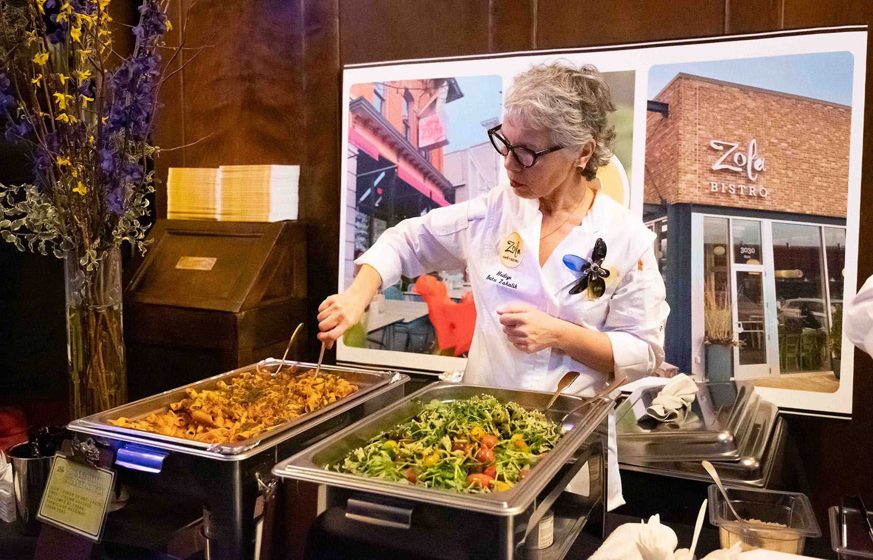 Hediye Batu Zakalik stands behind a banquet table and stirs a large pan of penne pasta.