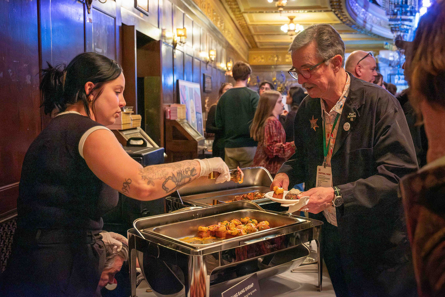 Valerie Egan stands behind a banquet table and serves shrimp from a large tray to Tom Bray.