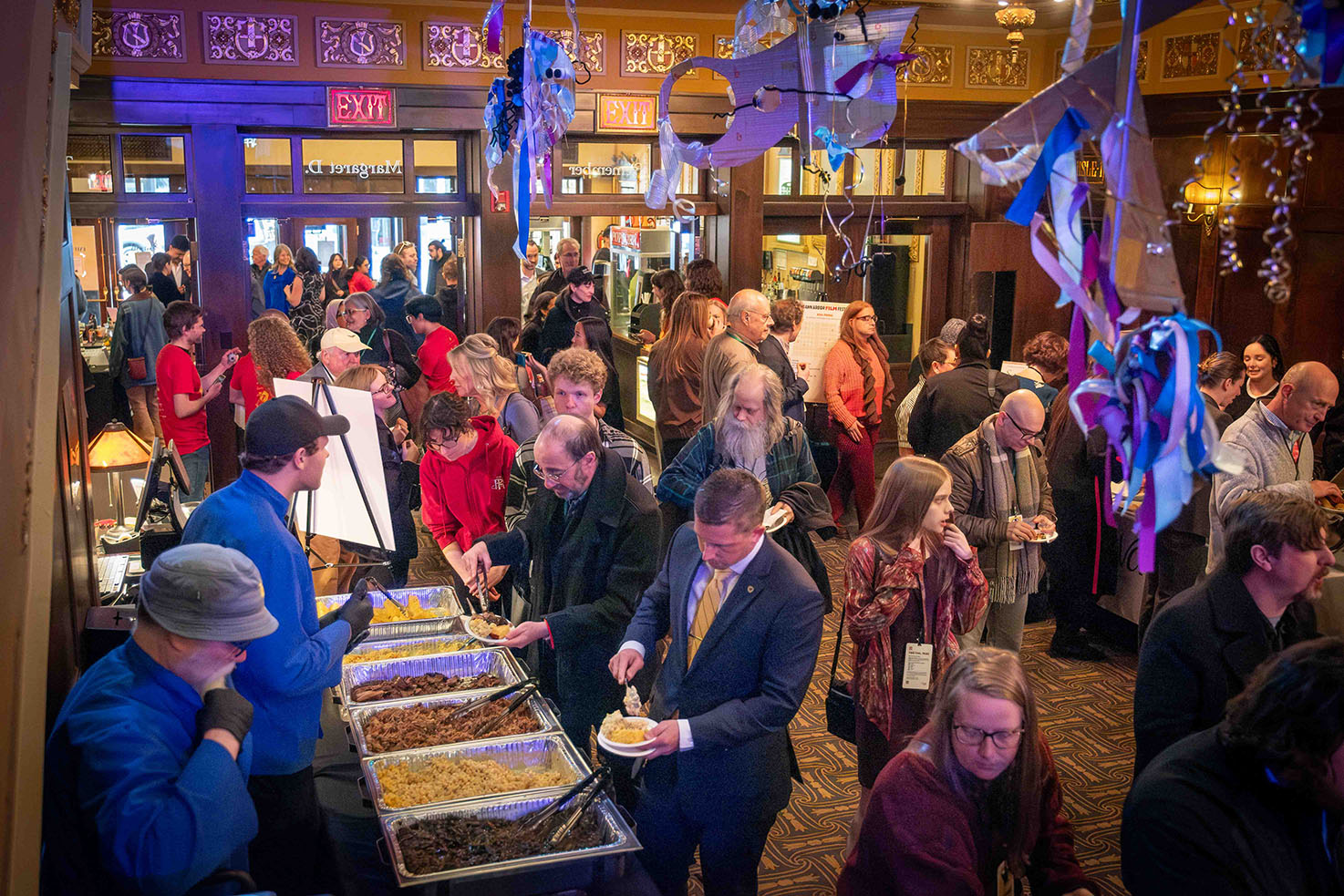 A banquet of food is shown with many people gathering and filling their plates.
