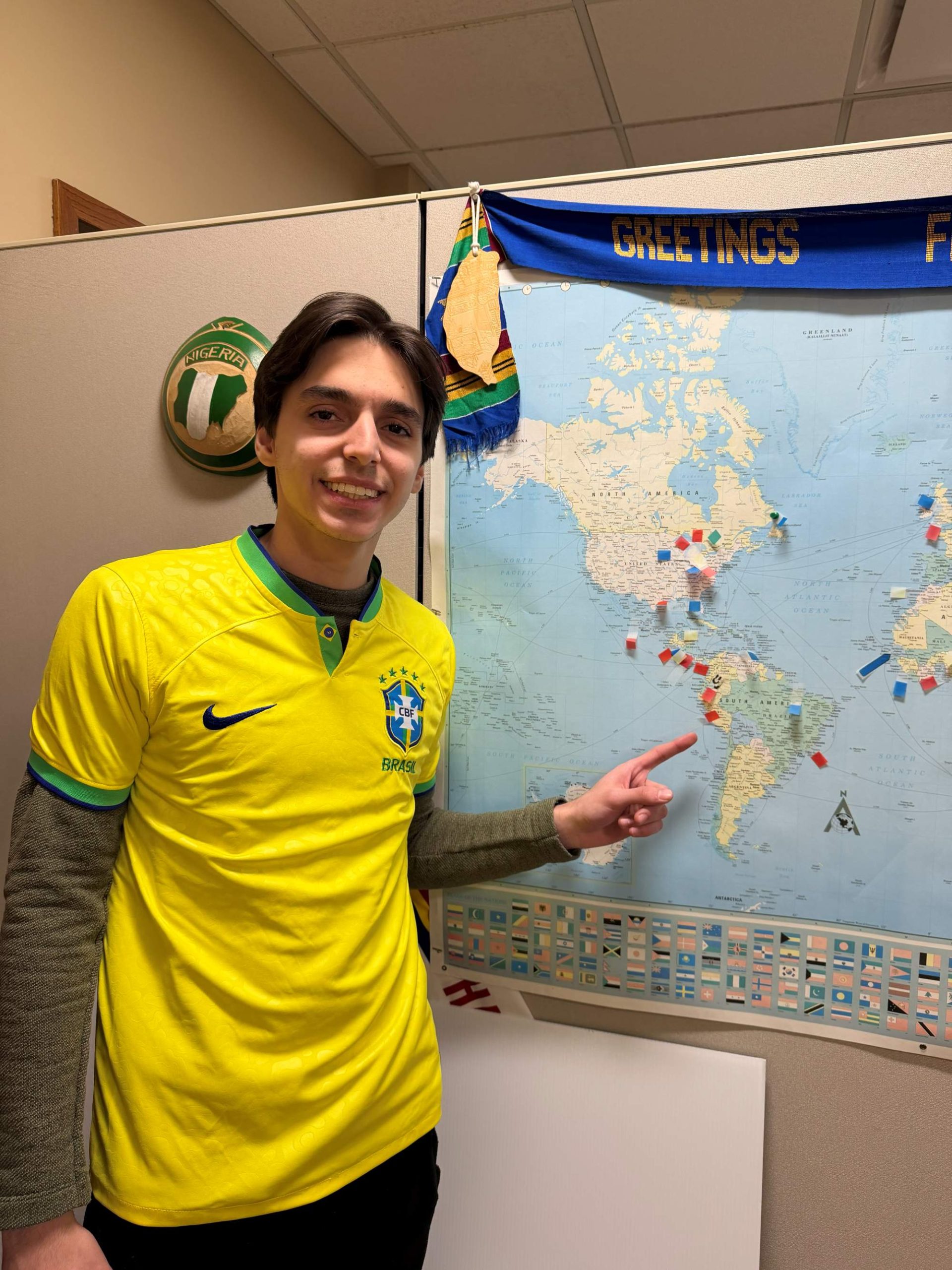 Felipe Carvalho Kalume stands in a yellow soccer jersey in front of a world map.