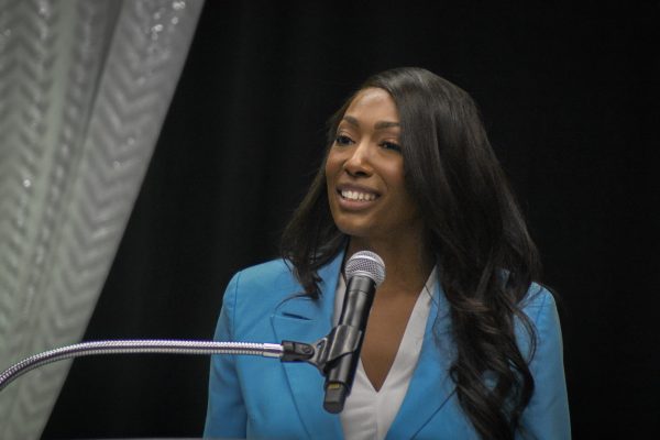 Aisha Bowe smiles and stands in front of a microphone.