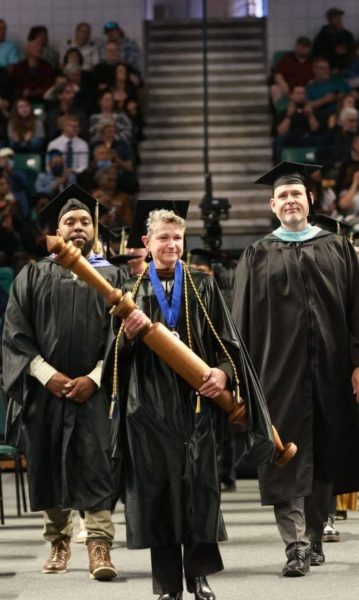 Washtenaw Community College faculty members leads a graduation ceremony. The women in front carries a ceremonial mace. 
