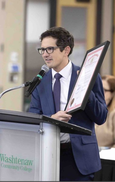 Jason Morgan stands at a podium holding up an award certificate.